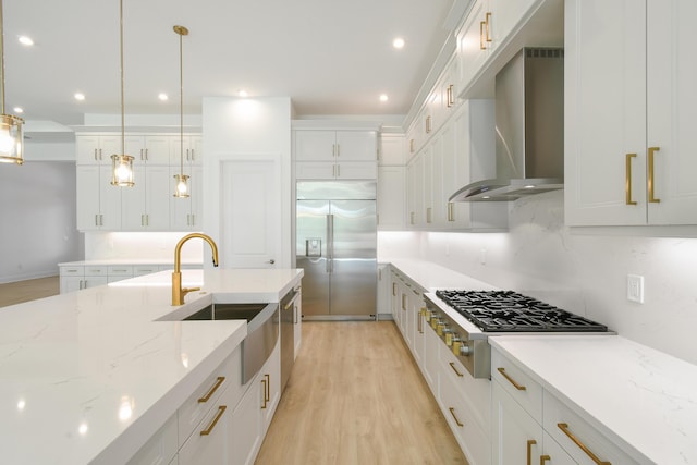 kitchen with hanging light fixtures, white cabinetry, appliances with stainless steel finishes, and wall chimney range hood