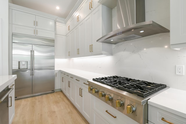 kitchen with wall chimney exhaust hood, white cabinetry, stainless steel appliances, and decorative backsplash