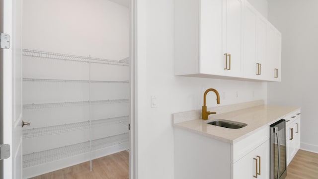 interior space with white cabinetry, light hardwood / wood-style floors, sink, and wine cooler