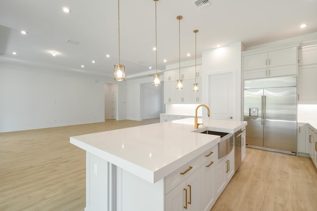 kitchen with built in fridge, decorative light fixtures, sink, white cabinets, and a large island with sink