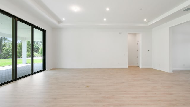 spare room with a tray ceiling and light hardwood / wood-style floors