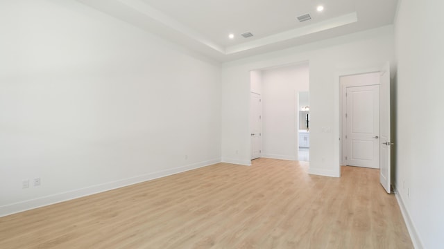 spare room with a towering ceiling, a tray ceiling, and light wood-type flooring