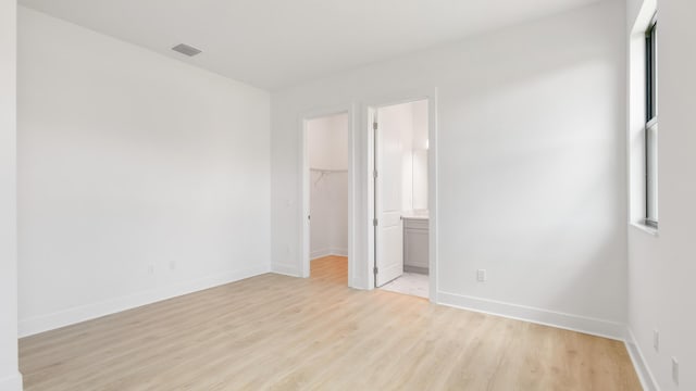 unfurnished bedroom featuring a closet, a walk in closet, ensuite bathroom, and light hardwood / wood-style flooring