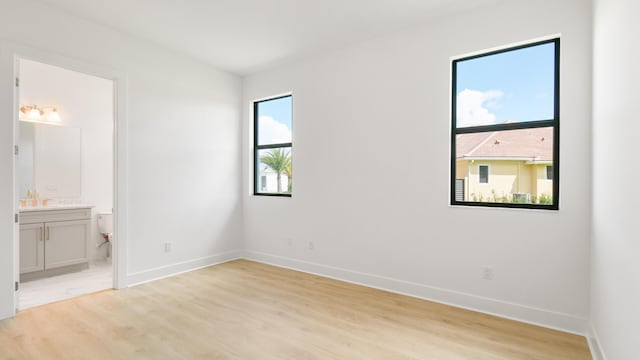 unfurnished bedroom featuring ensuite bathroom and light hardwood / wood-style flooring