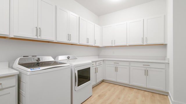 clothes washing area featuring cabinets, washing machine and clothes dryer, and light hardwood / wood-style flooring