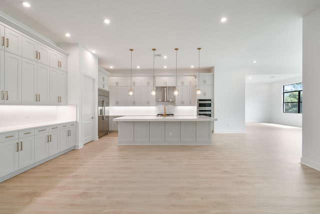 kitchen featuring pendant lighting, appliances with stainless steel finishes, an island with sink, and light wood-type flooring