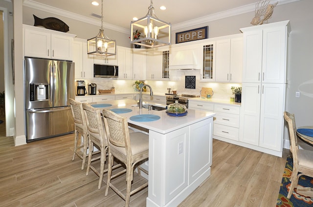 kitchen featuring custom exhaust hood, white cabinetry, an island with sink, pendant lighting, and stainless steel appliances