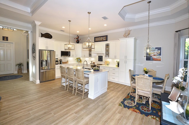 kitchen featuring a breakfast bar, white cabinetry, hanging light fixtures, stainless steel appliances, and a center island with sink