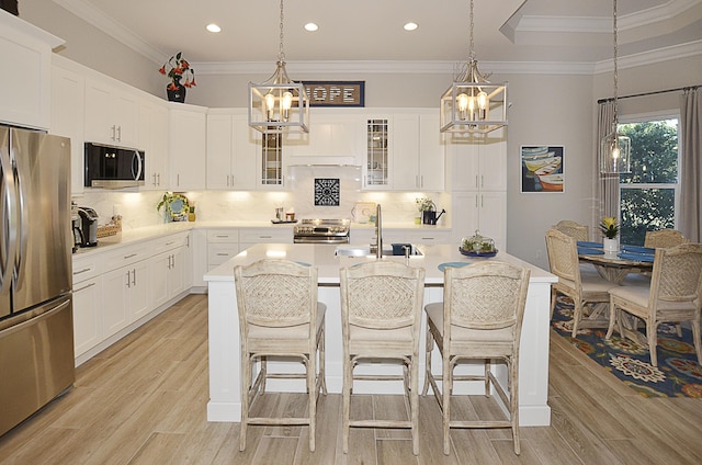 kitchen with white cabinets, stainless steel appliances, a kitchen island with sink, and backsplash