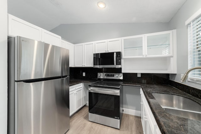 kitchen with sink, vaulted ceiling, dark stone countertops, stainless steel appliances, and white cabinets