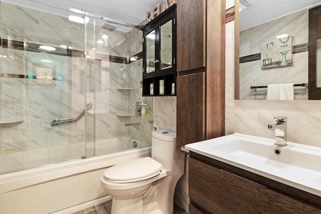 full bathroom with tasteful backsplash, tile walls, shower / bath combination with glass door, vanity, and toilet