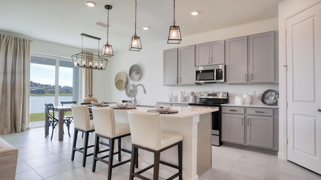 kitchen featuring a water view, stainless steel appliances, an island with sink, and gray cabinetry