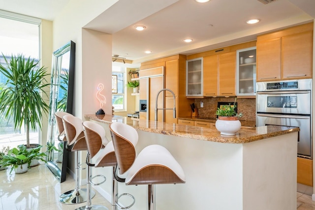 kitchen featuring double oven, a breakfast bar area, decorative backsplash, light stone counters, and paneled refrigerator