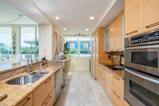 kitchen with sink, stainless steel appliances, tasteful backsplash, light stone countertops, and light brown cabinets