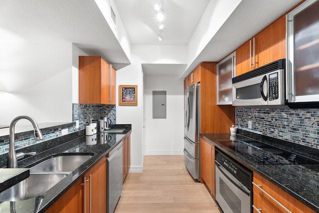 kitchen featuring sink, dark stone countertops, stainless steel appliances, track lighting, and light wood-type flooring