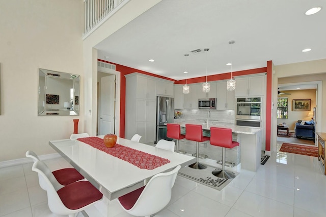 tiled dining area with ceiling fan, sink, and a towering ceiling