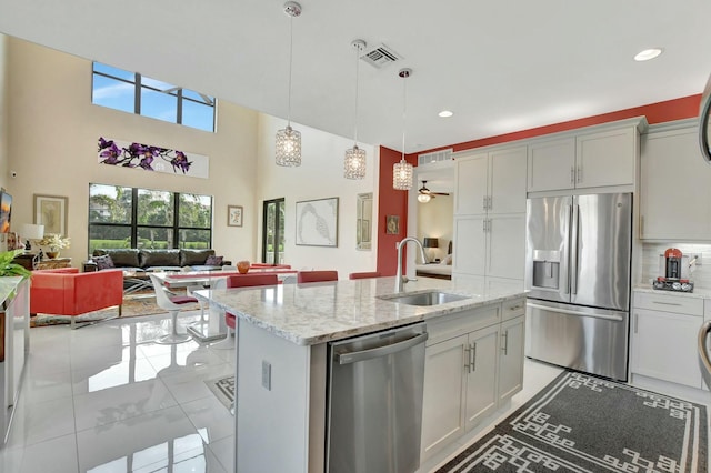 kitchen featuring sink, light stone counters, hanging light fixtures, appliances with stainless steel finishes, and a kitchen island with sink