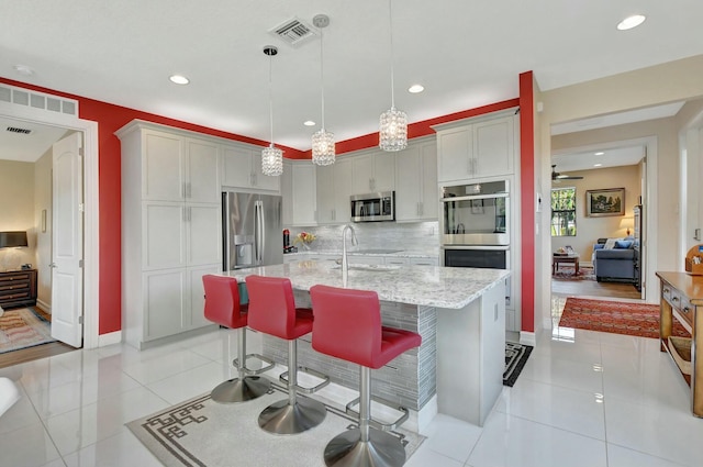 kitchen featuring appliances with stainless steel finishes, decorative light fixtures, sink, light tile patterned floors, and a center island with sink