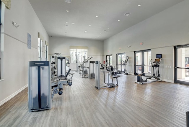 gym featuring a towering ceiling and light hardwood / wood-style floors