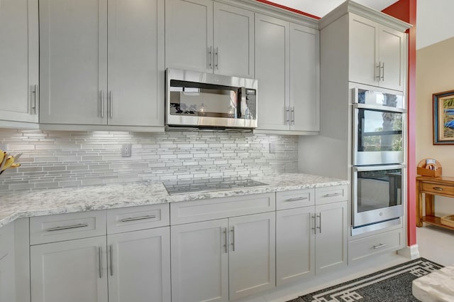 kitchen with tasteful backsplash, light stone countertops, stainless steel appliances, and gray cabinetry