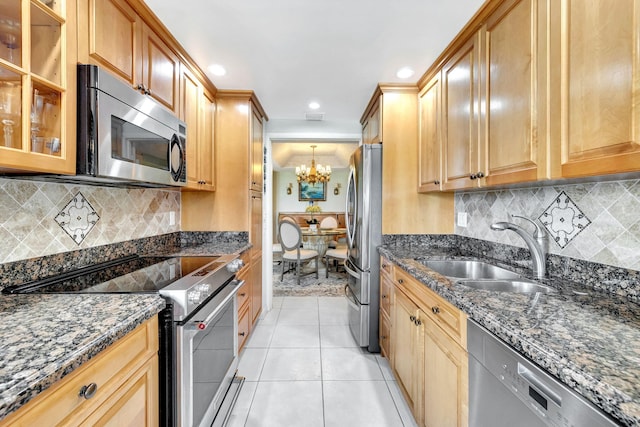 kitchen featuring appliances with stainless steel finishes, sink, dark stone countertops, and an inviting chandelier