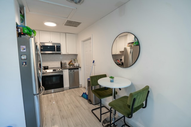 kitchen with stainless steel appliances, tasteful backsplash, white cabinets, and light hardwood / wood-style floors