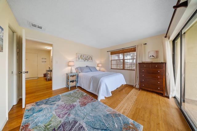 bedroom featuring baseboards, visible vents, a textured ceiling, and light wood-style floors