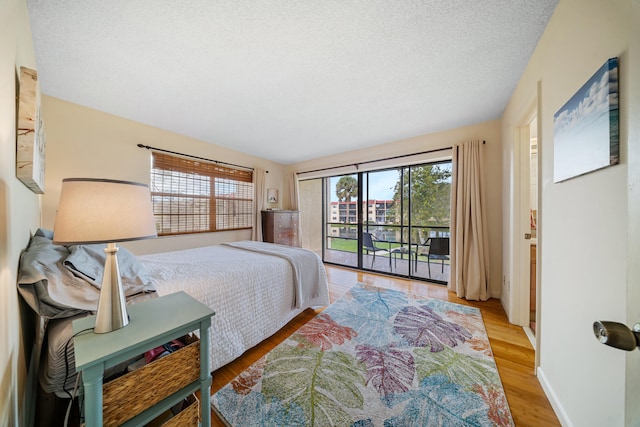 bedroom with baseboards, a textured ceiling, light wood-style flooring, and access to outside