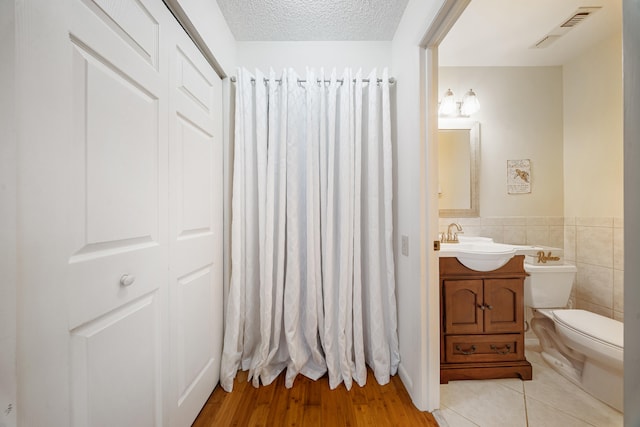 bathroom featuring visible vents, tile walls, toilet, vanity, and a textured ceiling