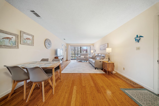 dining space featuring a textured ceiling, baseboards, visible vents, and light wood-type flooring