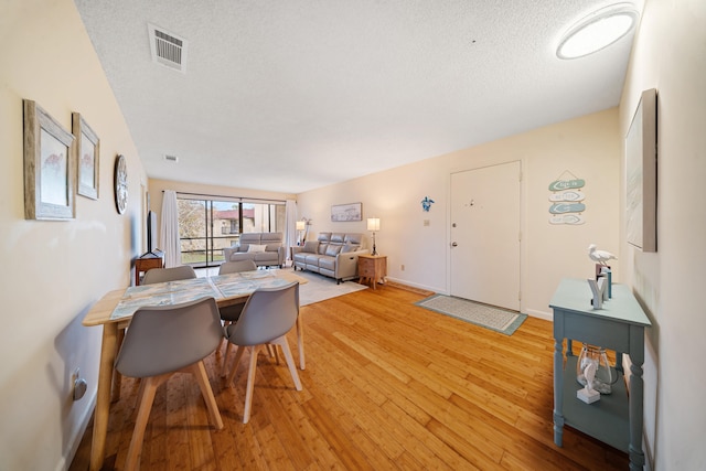 dining area featuring light wood-type flooring, baseboards, a textured ceiling, and visible vents