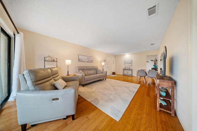 living area featuring a textured ceiling, visible vents, and light wood-type flooring