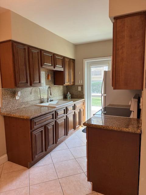 kitchen featuring light tile patterned floors, backsplash, stove, a sink, and light stone countertops