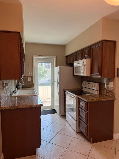 kitchen featuring dark stone countertops, white appliances, a sink, and decorative backsplash