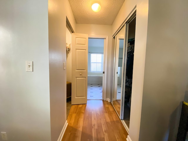 hall with a textured ceiling, light wood finished floors, and baseboards