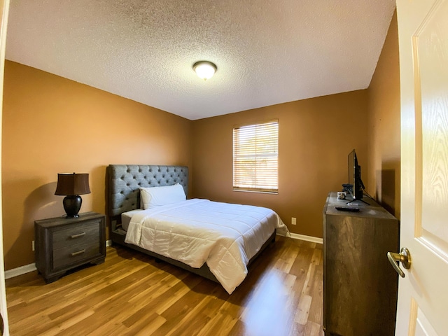 bedroom with a textured ceiling, baseboards, and wood finished floors