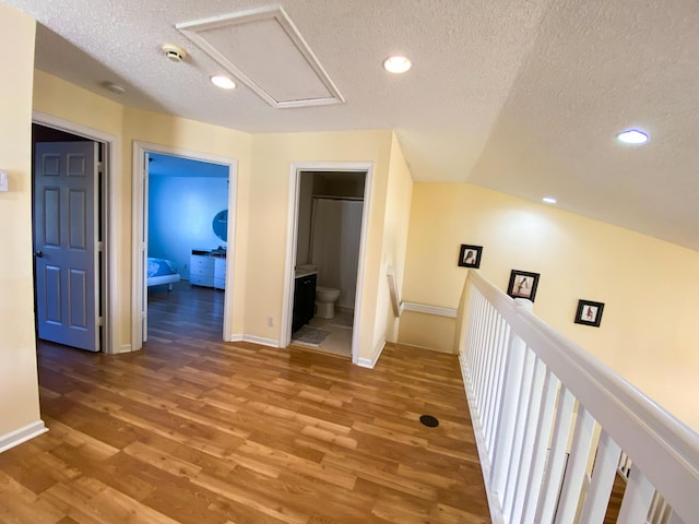 hall with recessed lighting, a textured ceiling, an upstairs landing, and wood finished floors