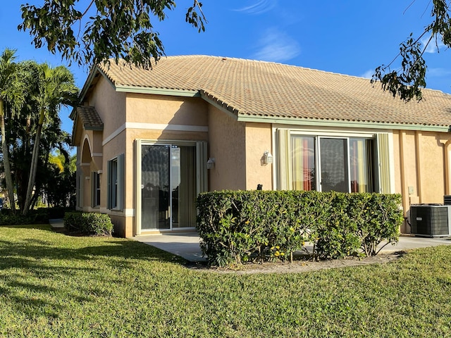 back of property featuring a tiled roof, a yard, central AC unit, and stucco siding