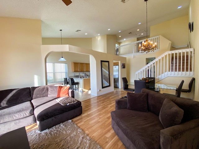 living area with arched walkways, stairs, light wood-style floors, high vaulted ceiling, and recessed lighting