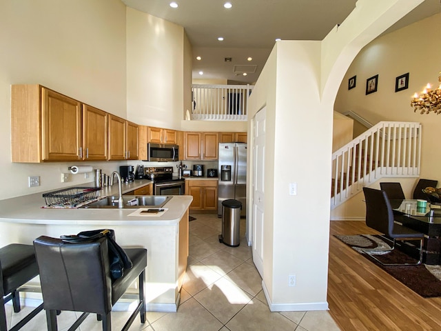 kitchen featuring light tile patterned floors, stainless steel appliances, light countertops, a peninsula, and a kitchen bar