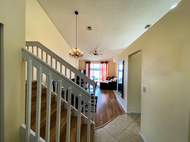 staircase featuring an inviting chandelier, visible vents, a textured ceiling, and tile patterned floors