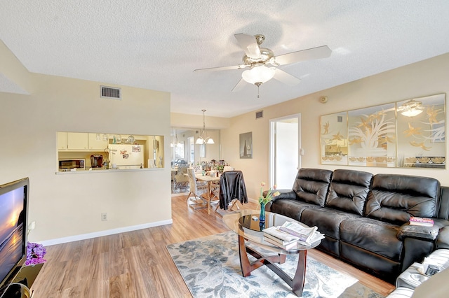 living room featuring ceiling fan with notable chandelier, a textured ceiling, and light hardwood / wood-style flooring