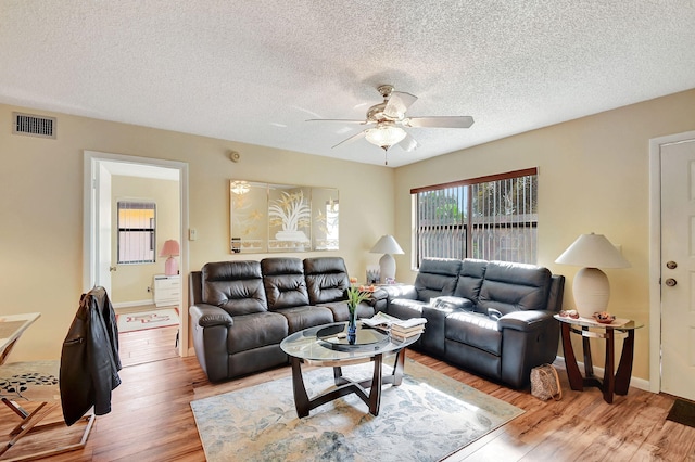 living room with ceiling fan, light hardwood / wood-style flooring, and a textured ceiling