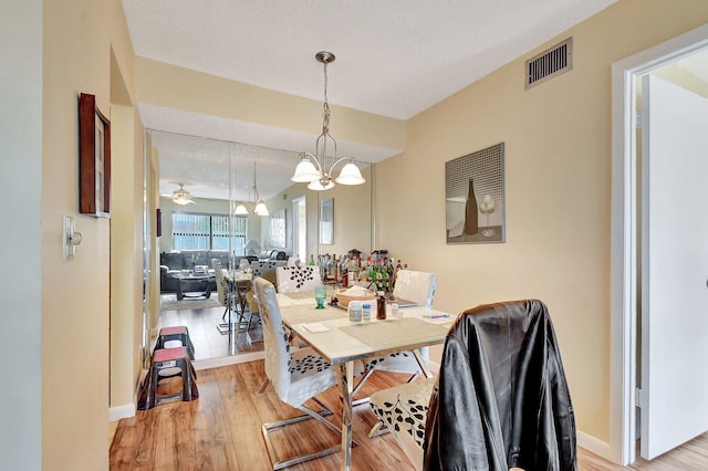 dining area featuring a chandelier, a textured ceiling, and light wood-type flooring