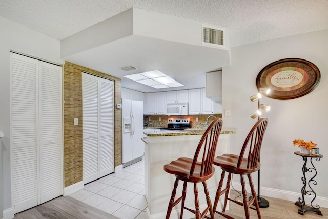 kitchen featuring tasteful backsplash, a textured ceiling, kitchen peninsula, white appliances, and white cabinets