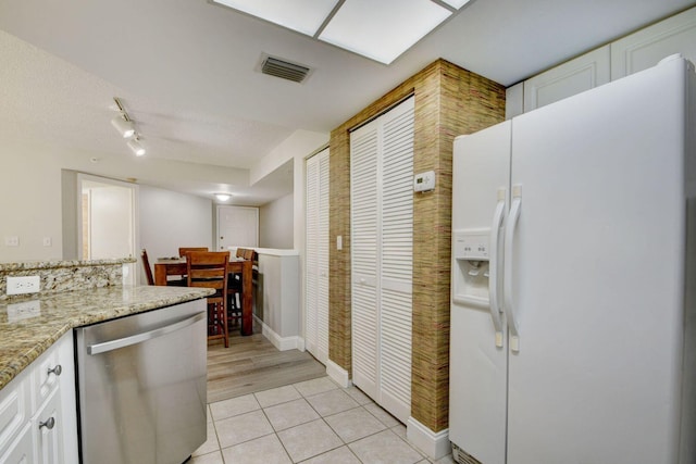 kitchen with light tile patterned floors, dishwasher, white refrigerator with ice dispenser, light stone countertops, and white cabinets