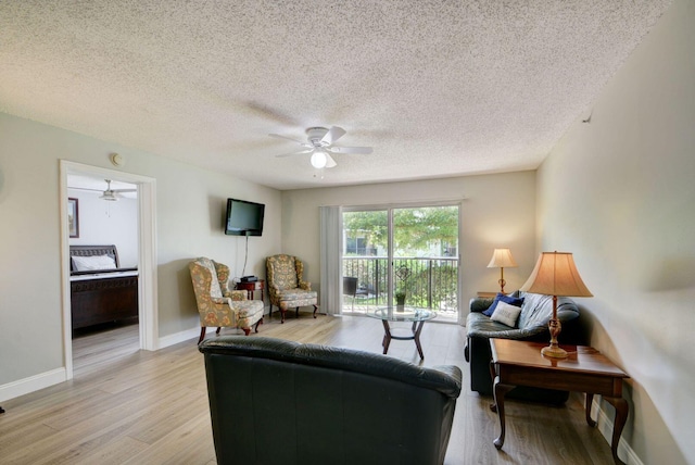 living room with ceiling fan, light wood-type flooring, and a textured ceiling