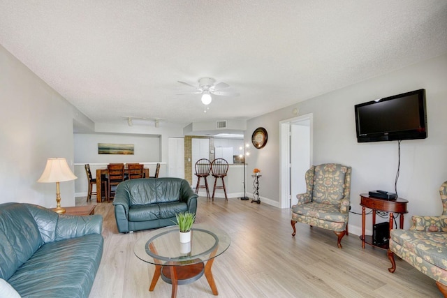 living room featuring ceiling fan, a textured ceiling, and light wood-type flooring