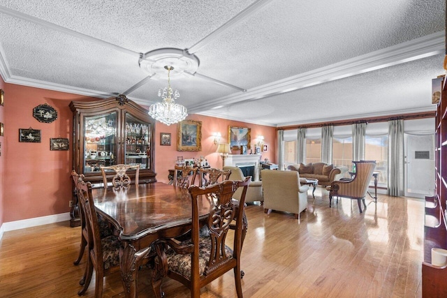 dining area with ornamental molding, a textured ceiling, a notable chandelier, and light hardwood / wood-style floors