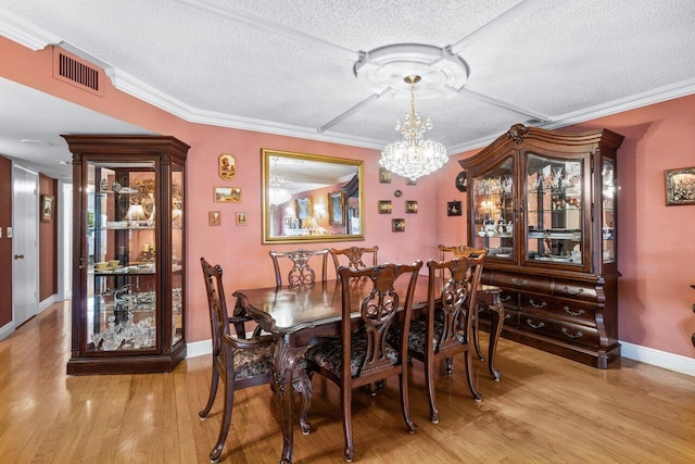 dining space featuring ornamental molding, a chandelier, a textured ceiling, and light wood-type flooring